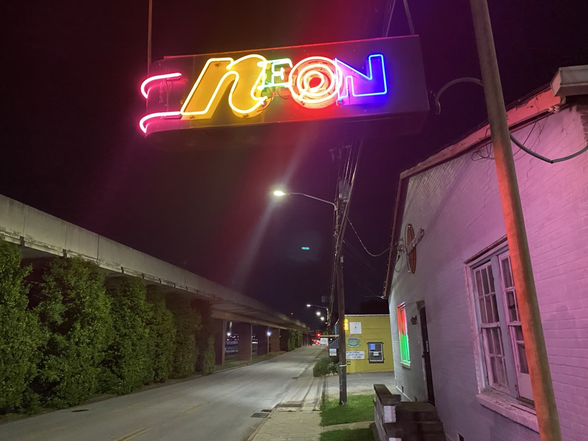 A glowing multicolored 'NEON' sign on a quiet street at night.